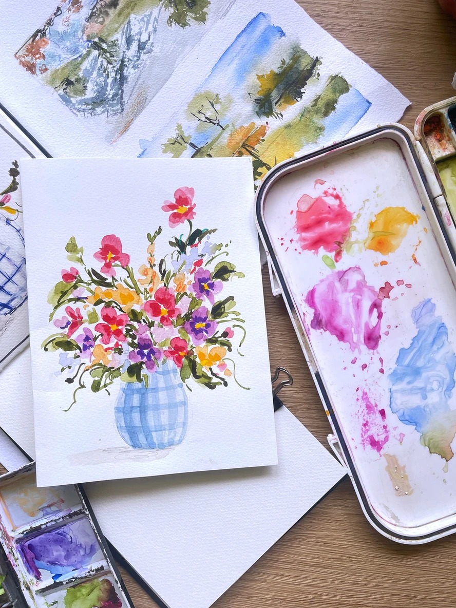 Watercolor bouquet in a gingham vase beside a paint palette
